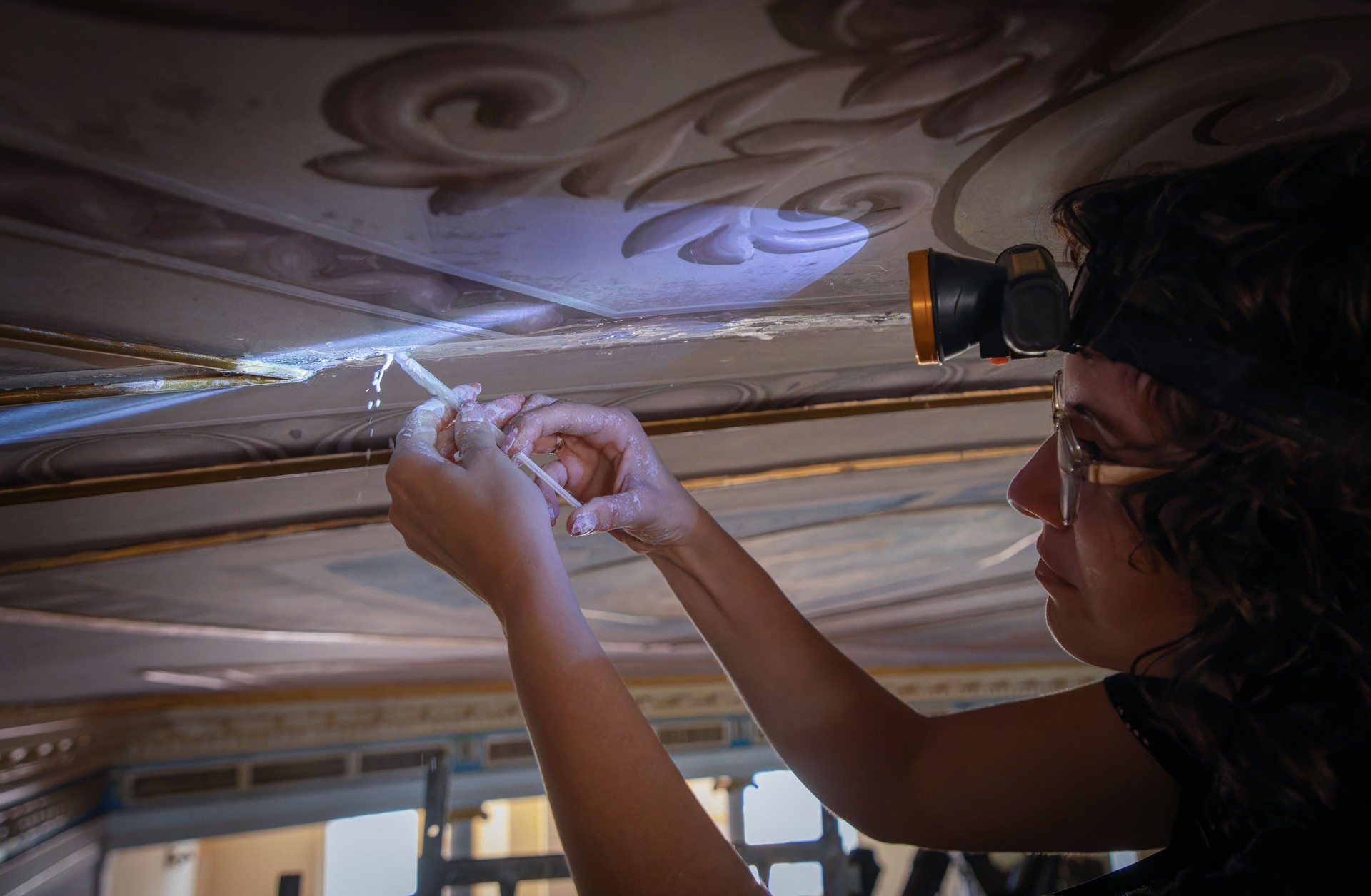Conservator restoring intricate ceiling art.