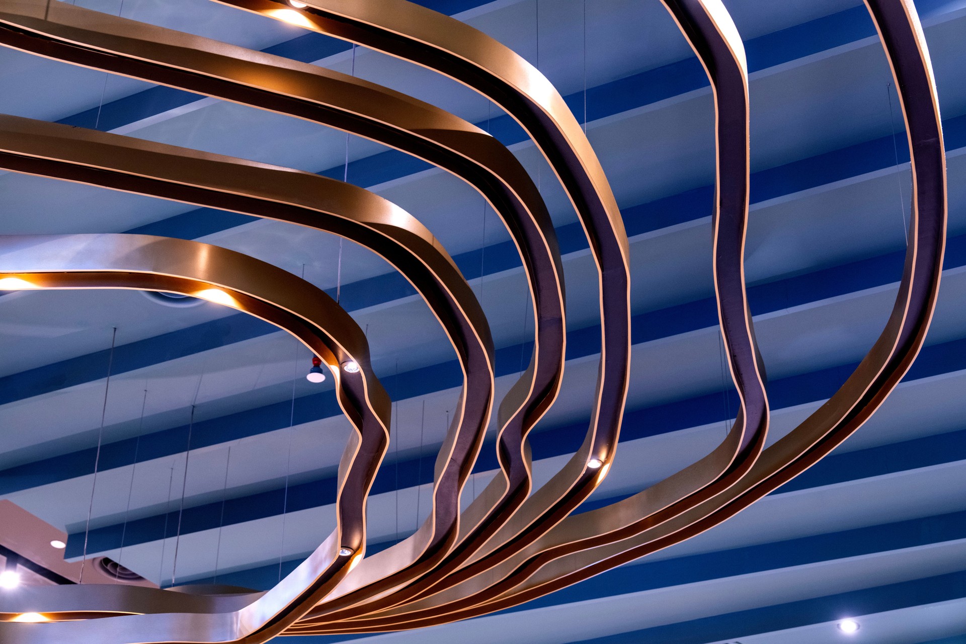 Suspended Elegance: Curved Bronze Forms Against a Striped Ceiling